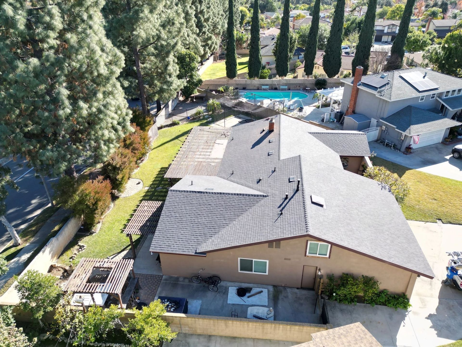 Aerial view of a suburban house with gray roof, backyard deck, pool, and tall trees nearby