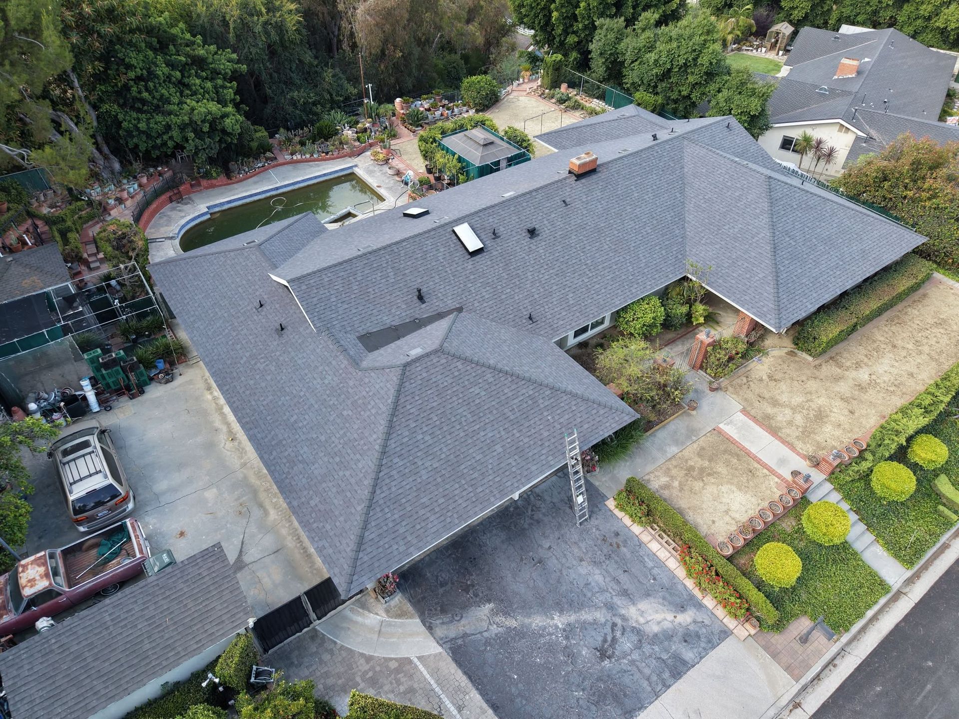 Aerial view of a large gray-roofed house with driveway, yard, and landscaped garden.