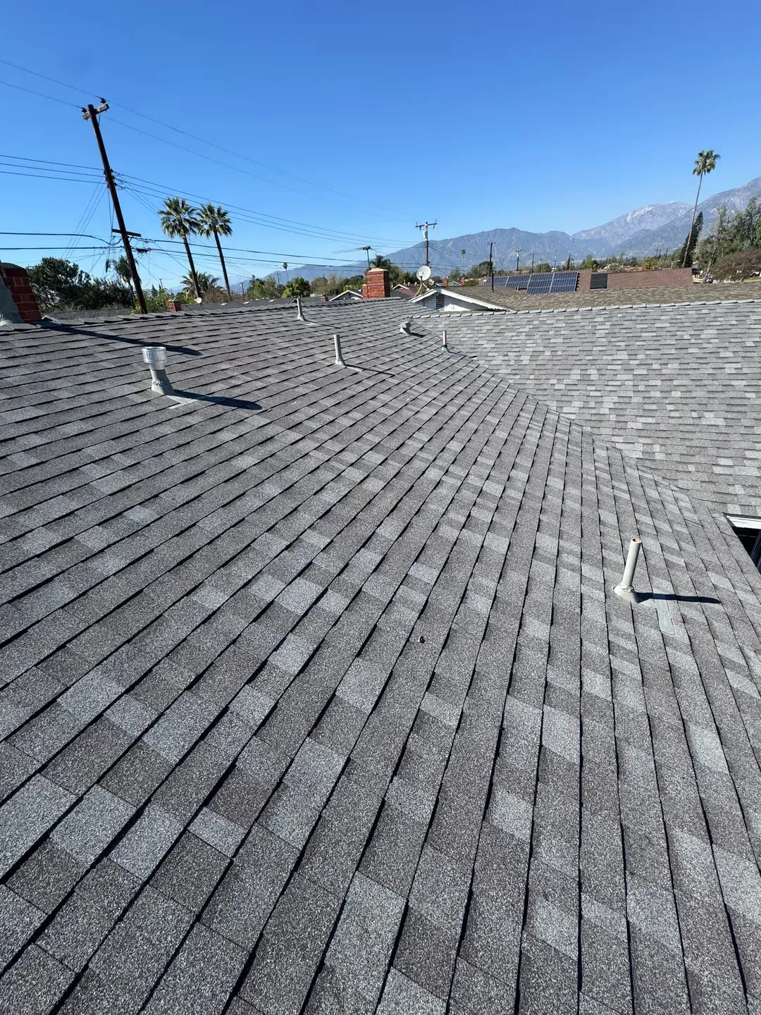 Shingled rooftop with desert mountains, palm trees, and clear blue sky in the background