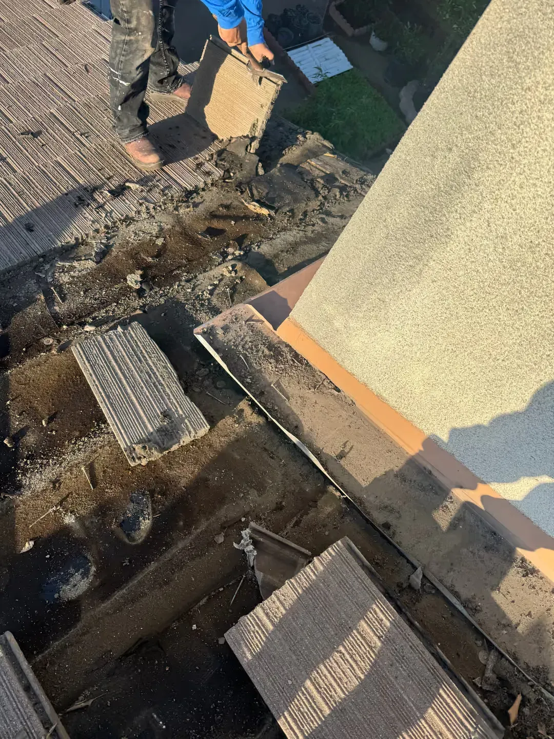 Roof damage with missing shingles and exposed underlayment beside a wall and gutter area