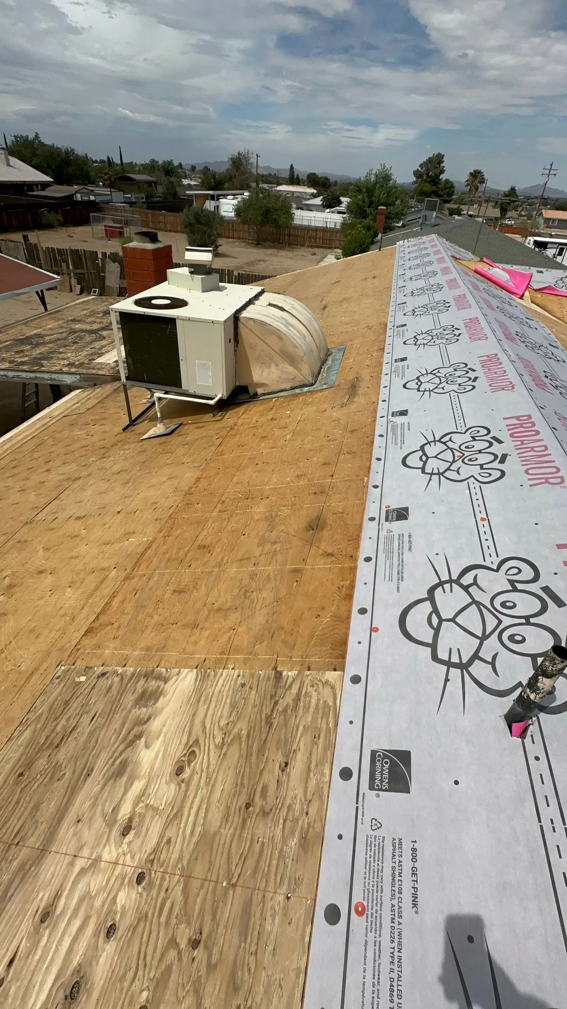 Rooftop with workers’ materials, a white HVAC unit, and rolled roofing under construction with a city view.