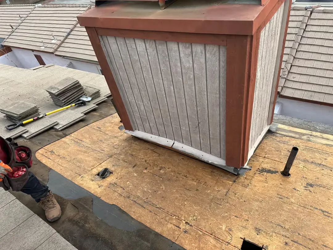 Roofing worker installing a small vented skylight on a shingled roof with plywood decking exposed