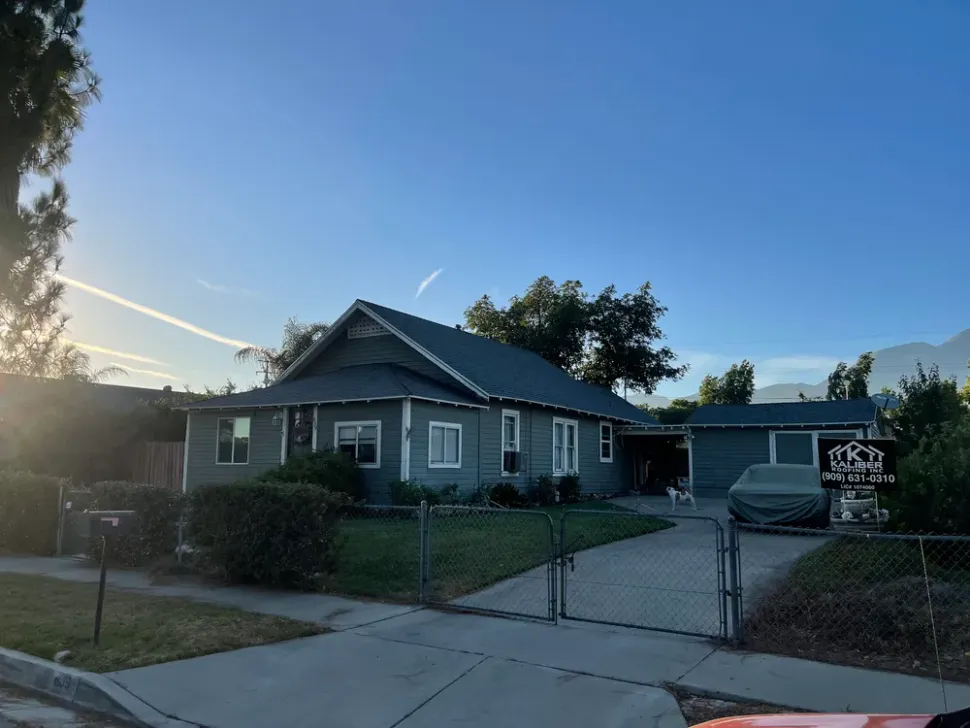 Single-story gray house with a chain-link fence and driveway at dusk under a clear blue sky