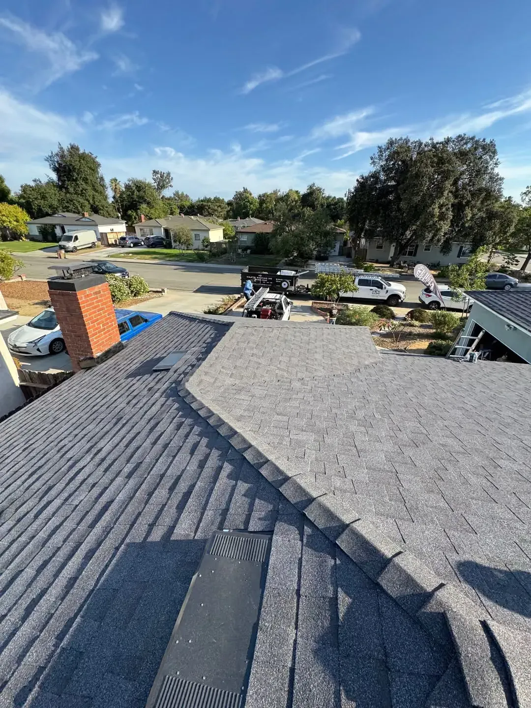 View from a roof over a suburban neighborhood, with gray shingles and a clear blue sky.