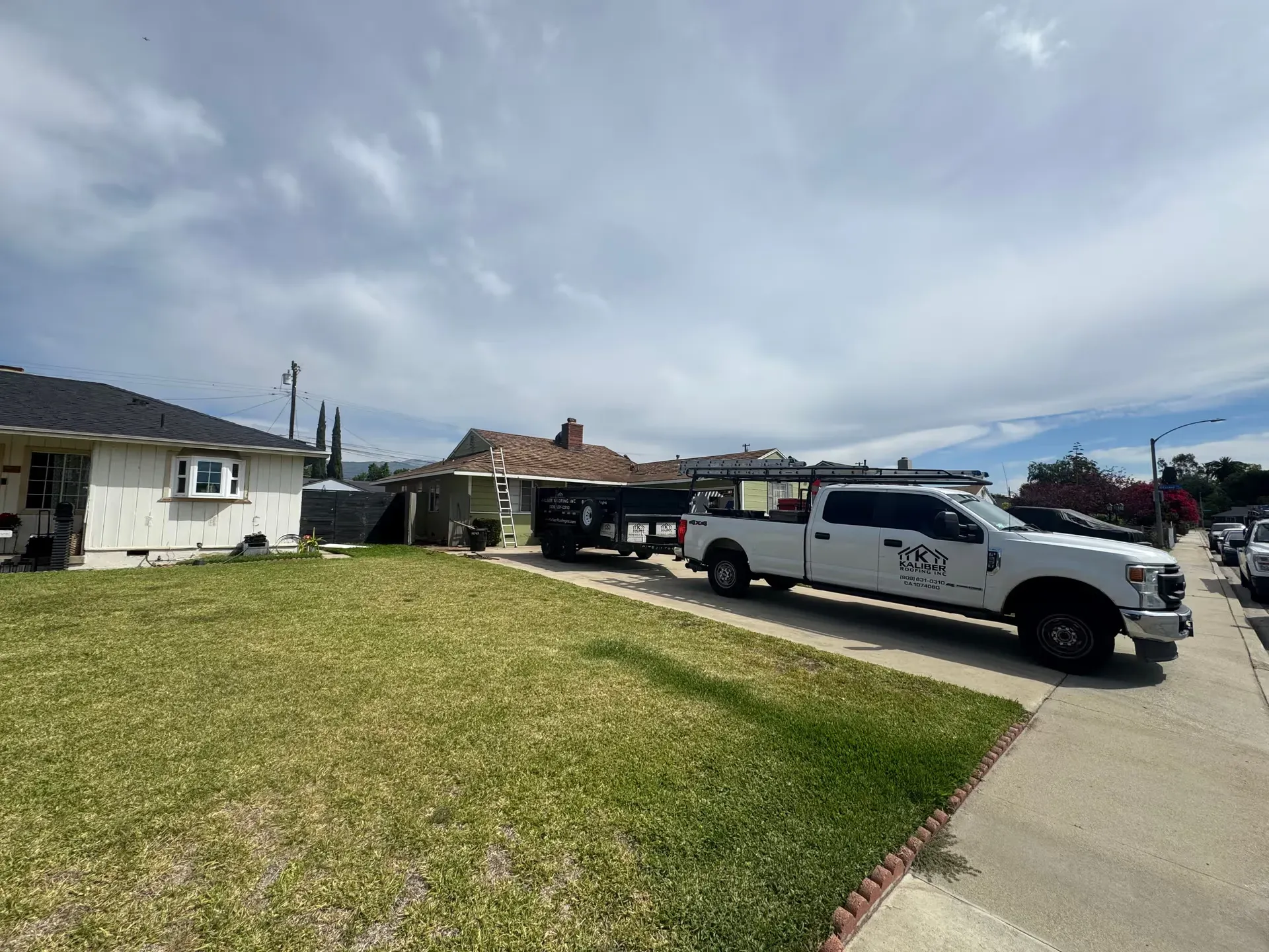 Suburban street with a white pickup truck parked beside a grassy yard and houses under a cloudy sky