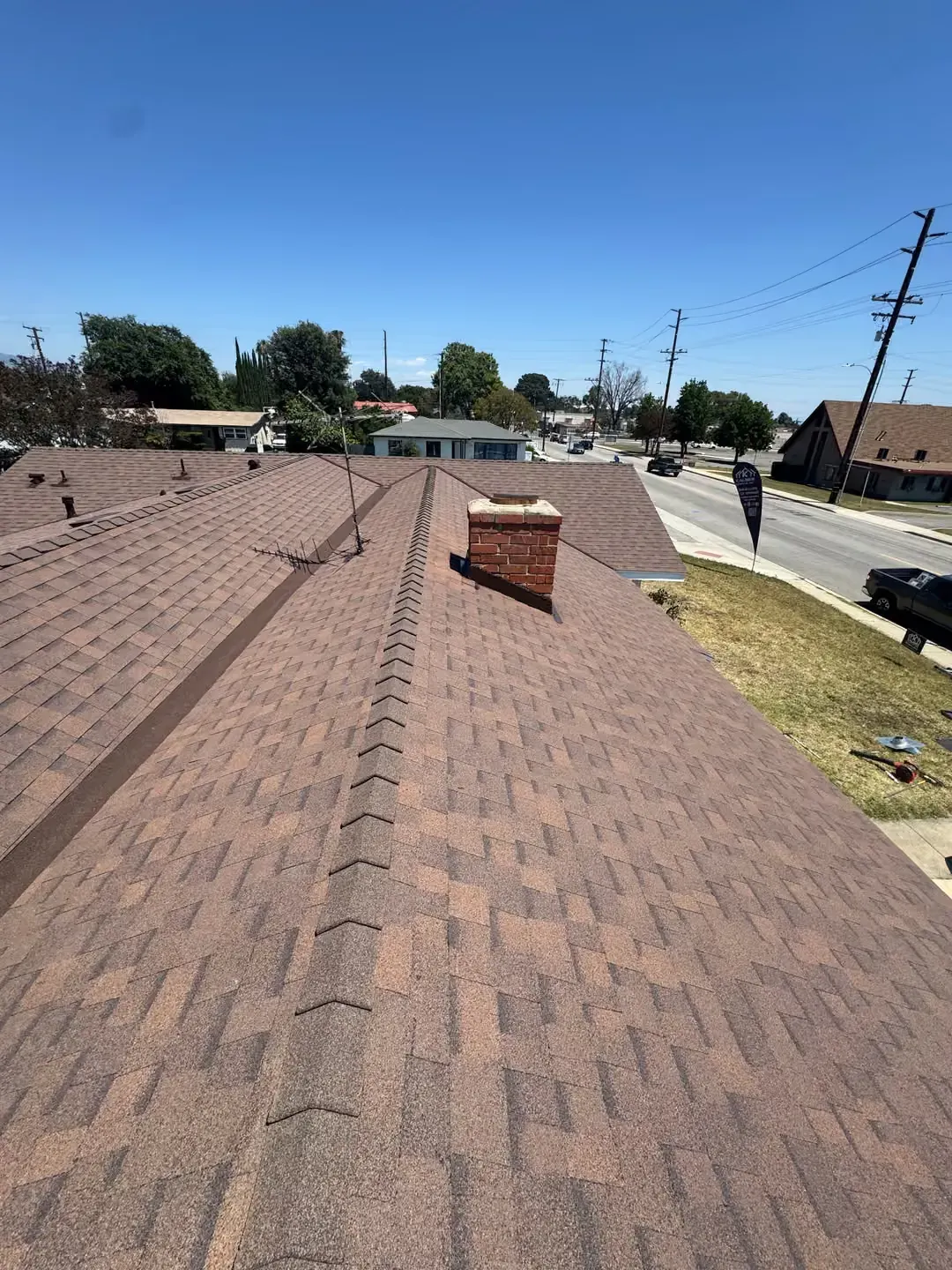 Rooftop with brown shingles, brick chimney, and a street with utility poles under a clear blue sky