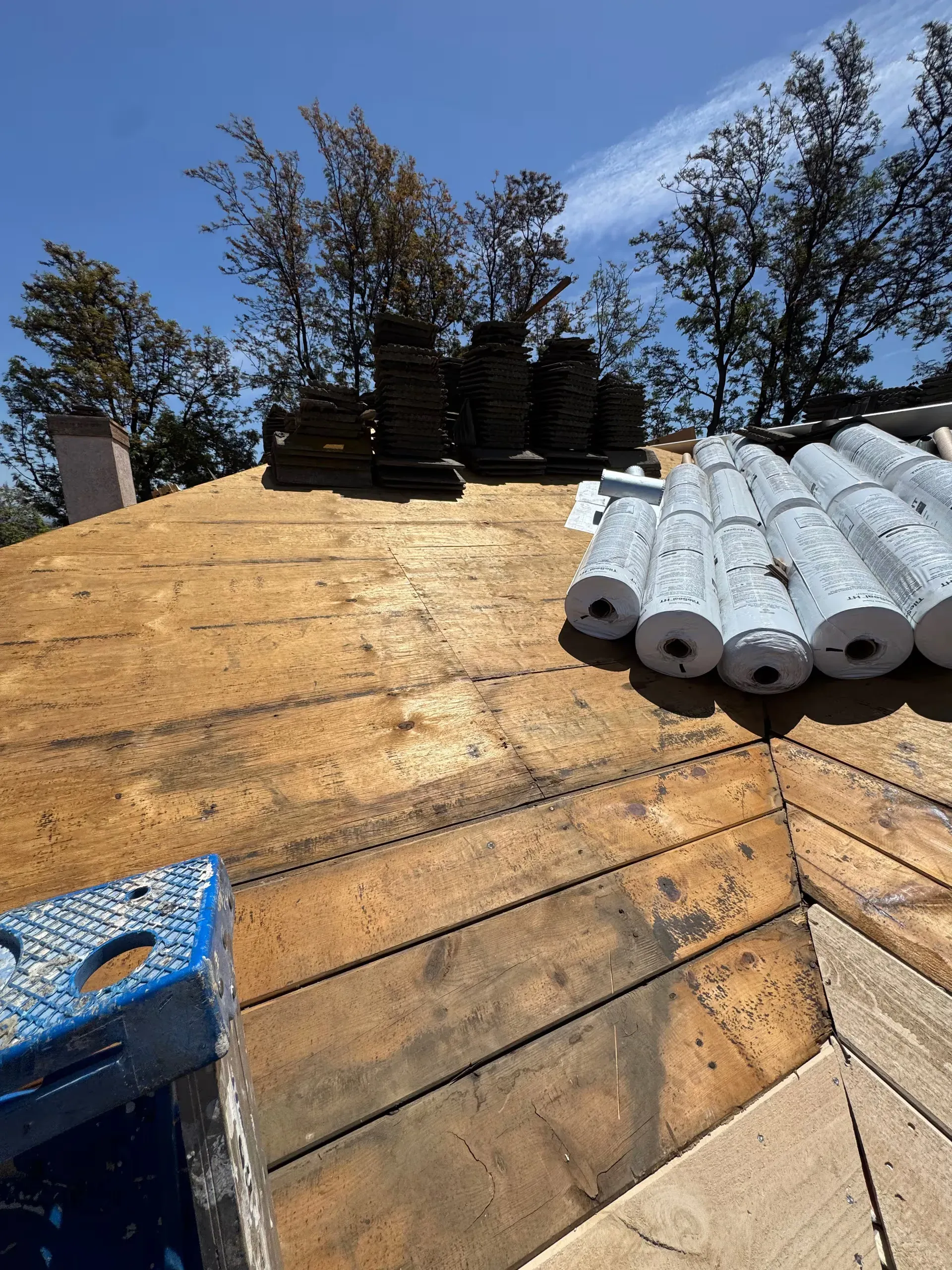 Roof under construction with stacked shingles and materials on a sloped roof under a blue sky