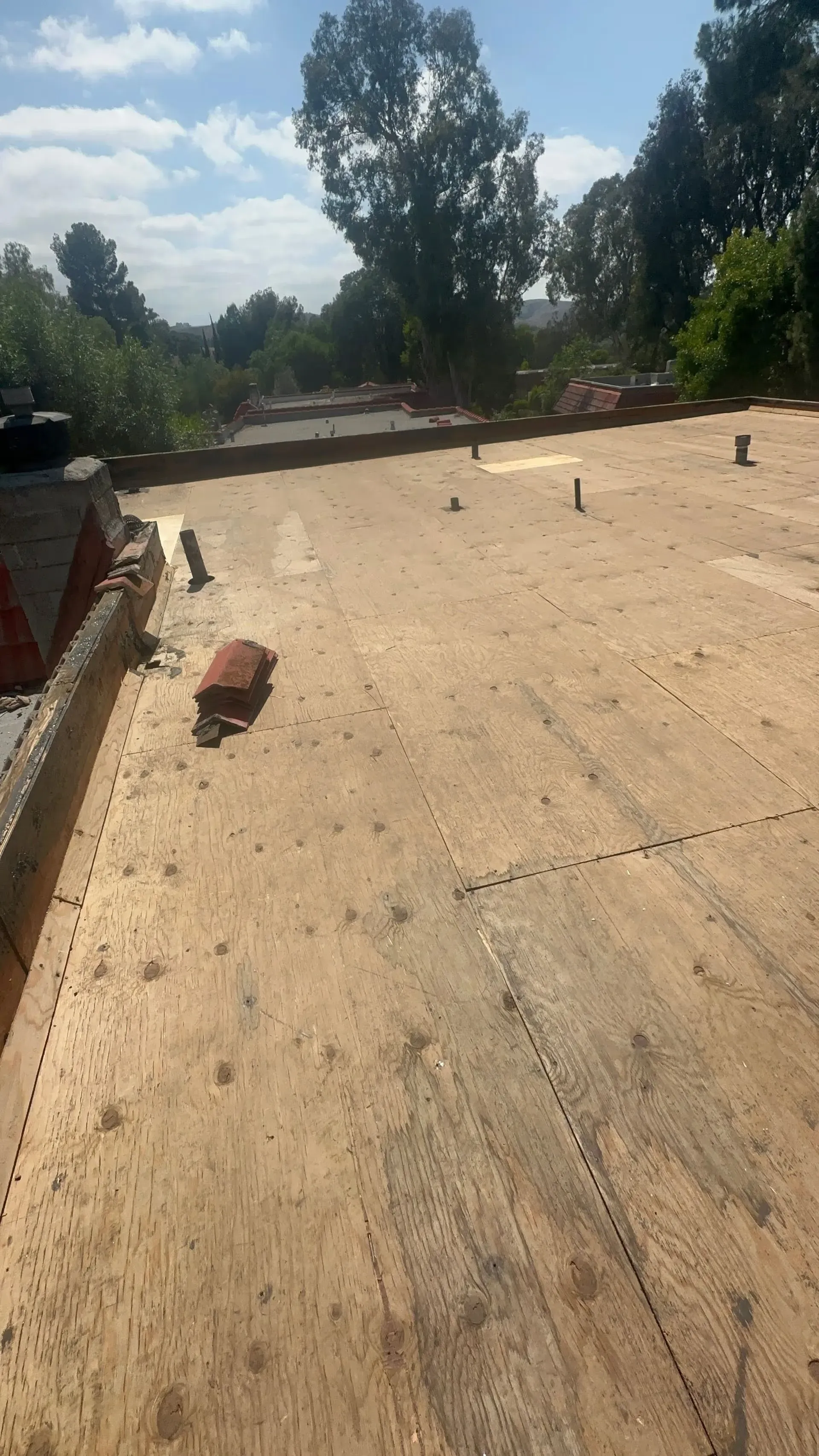 Rooftop under construction with plywood, scattered materials, and trees in the background