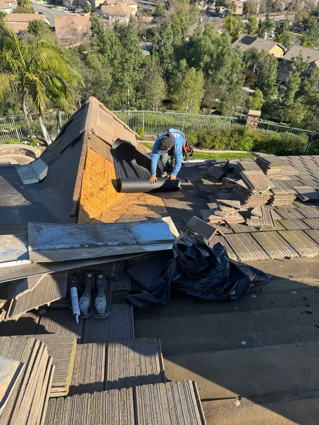 Worker repairing a rooftop dormer with trees and houses in the background