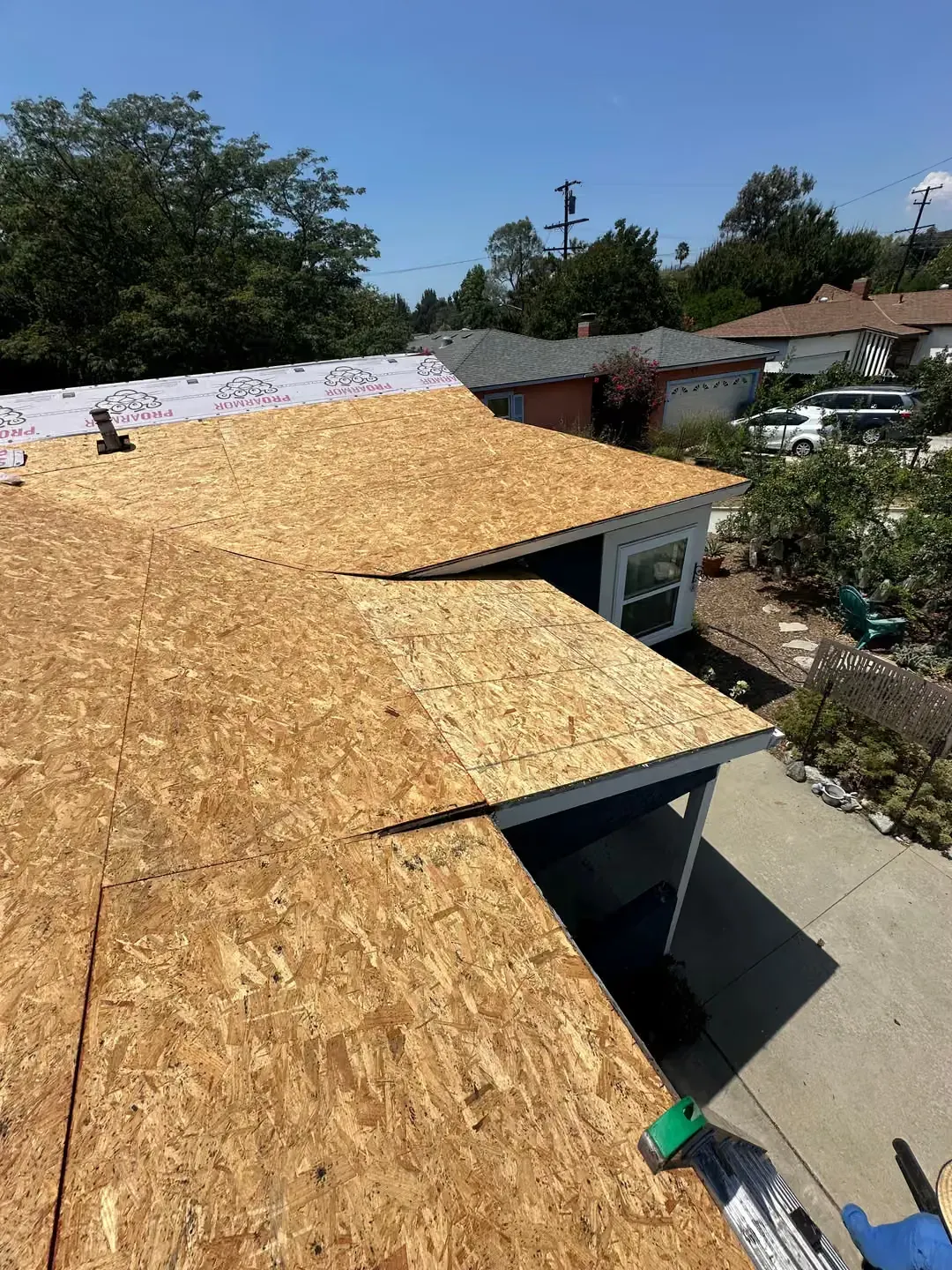 Roof under construction with plywood sheathing and a visible garage driveway below