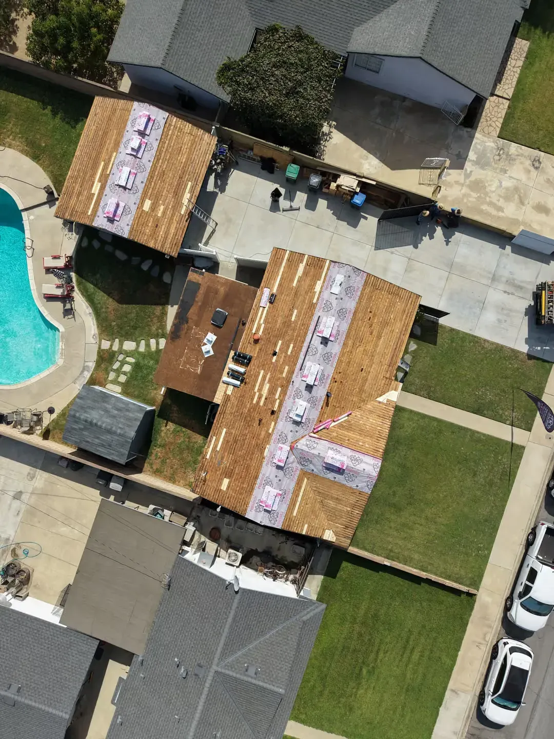 Aerial view of homes with damaged roofs and tarps, a backyard pool, and nearby parked cars.