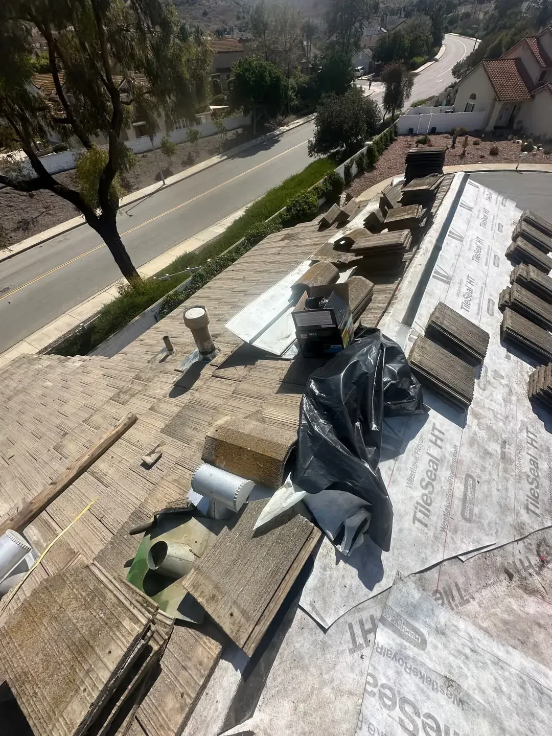 Rooftop with construction materials and tarps beside a road and trees below