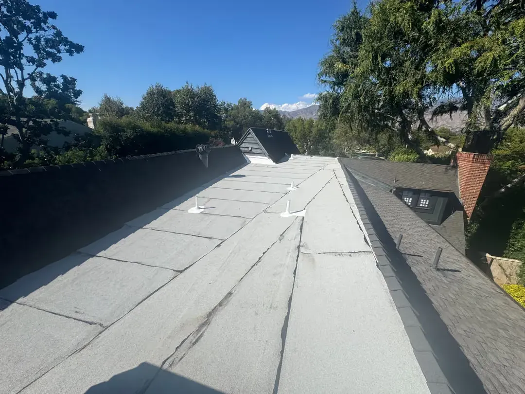 Rooftop with new gray shingles and blue sky, trees lining both sides.