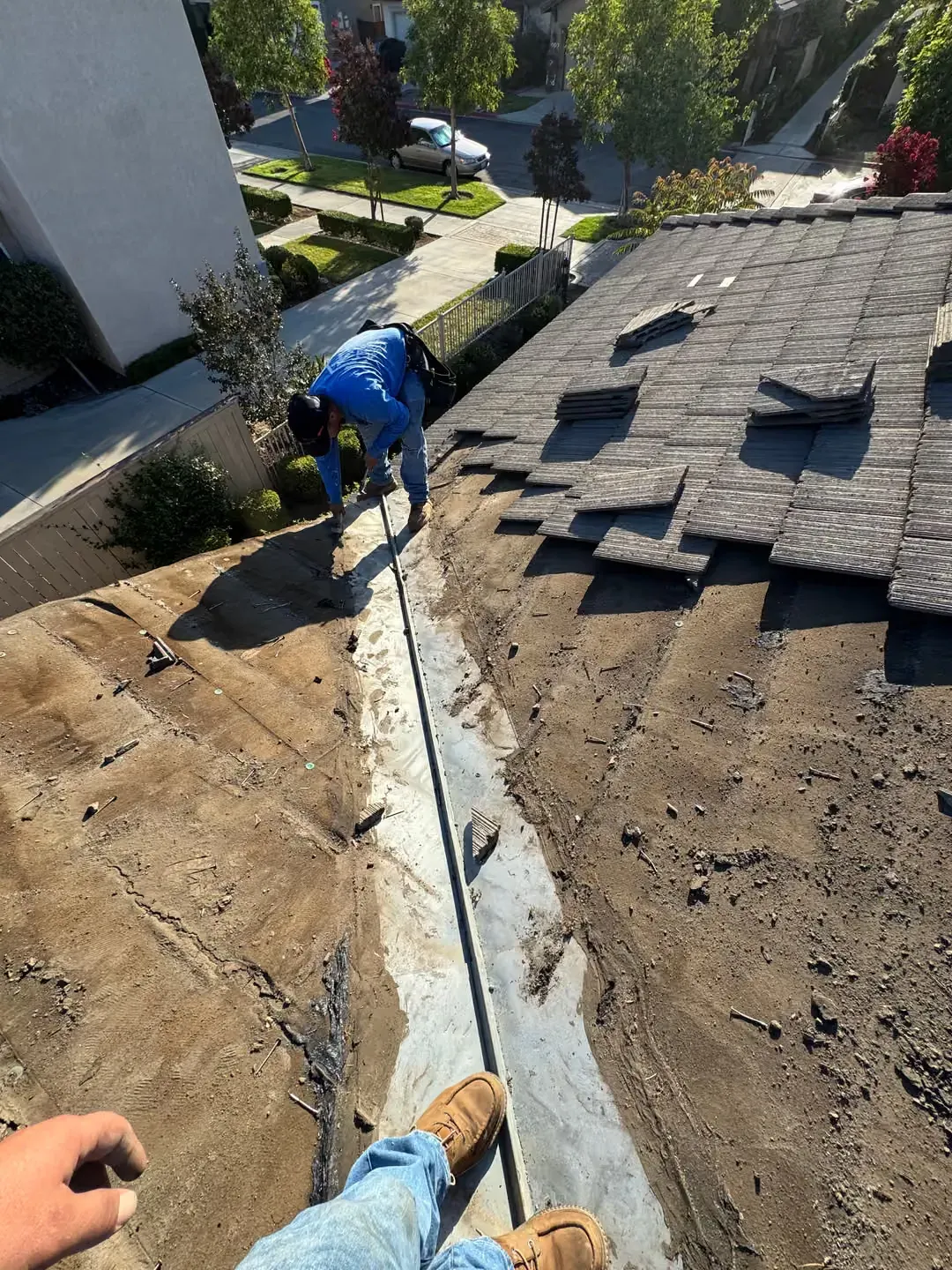 Worker installing roof shingles beside a metal flashing strip on a sloped rooftop