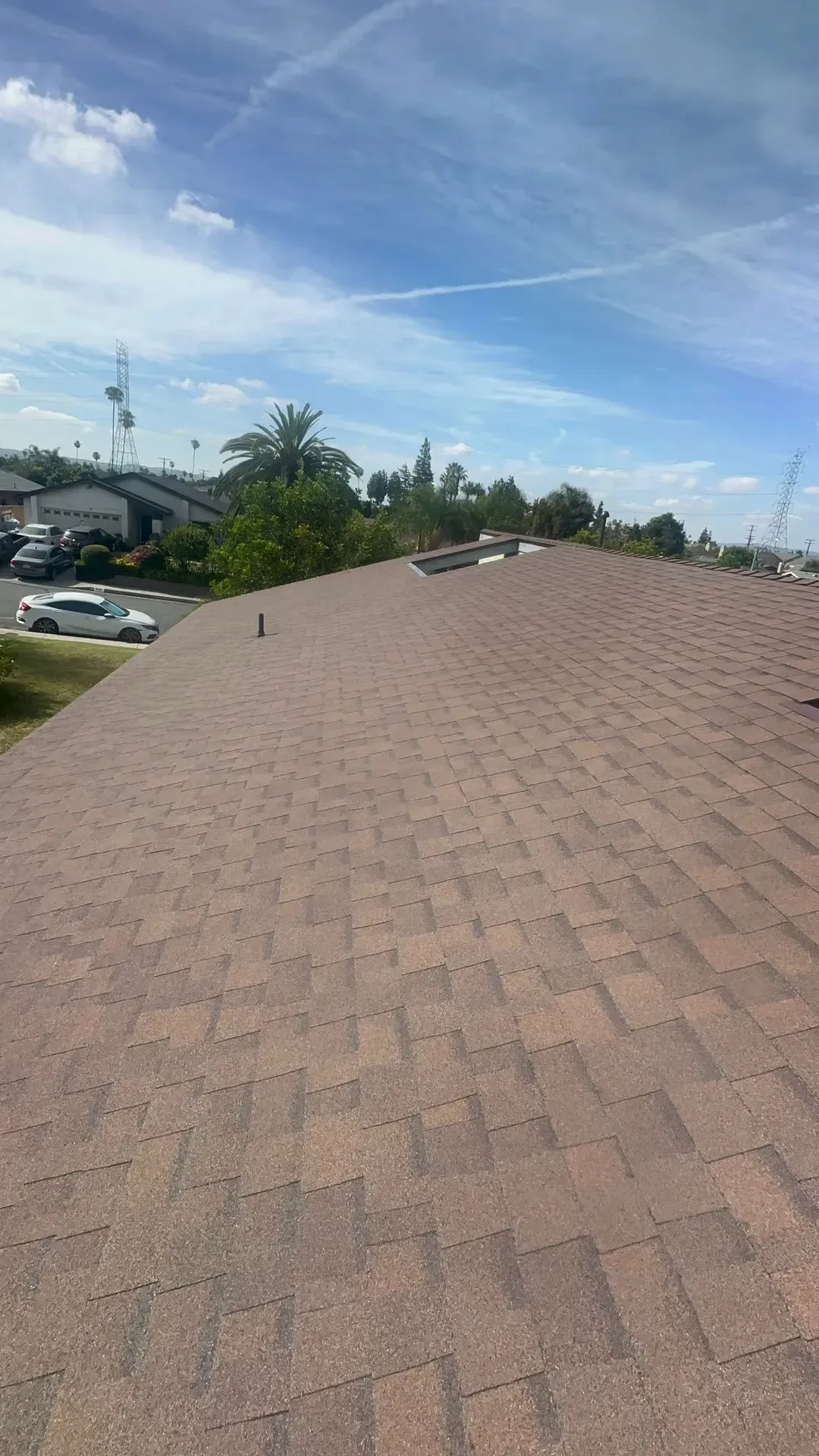 Rooftop with brown shingles overlooking a suburban street under a blue sky with wispy clouds