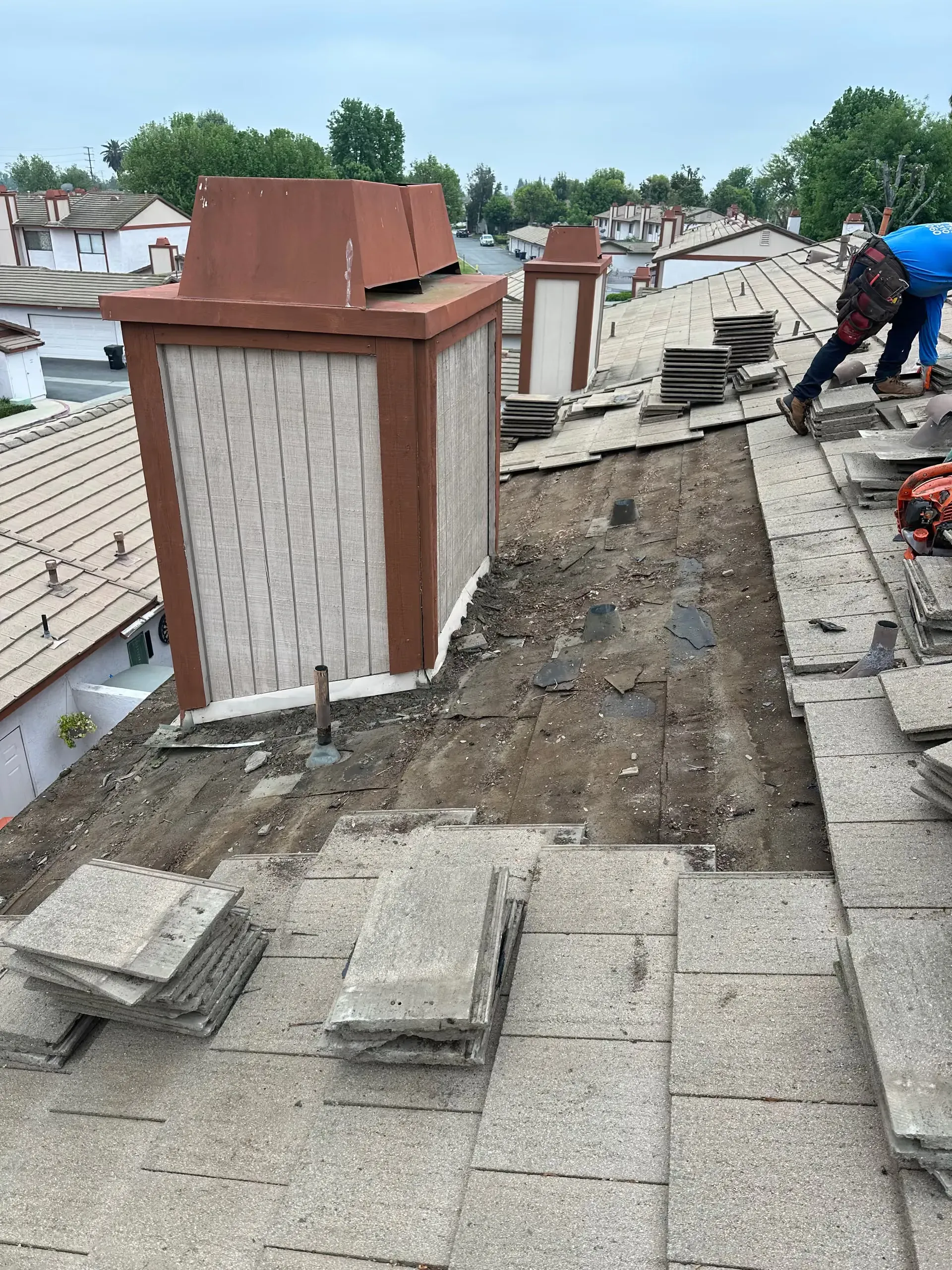 Damaged rooftop with exposed area, scattered tiles, and workers repairing the roof.