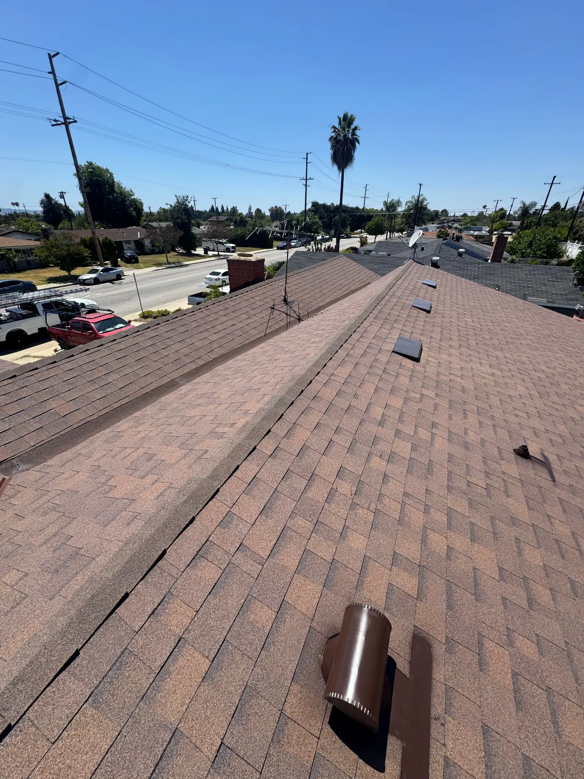 Rooftop shingles with vents, overlooking a residential neighborhood under a clear blue sky.