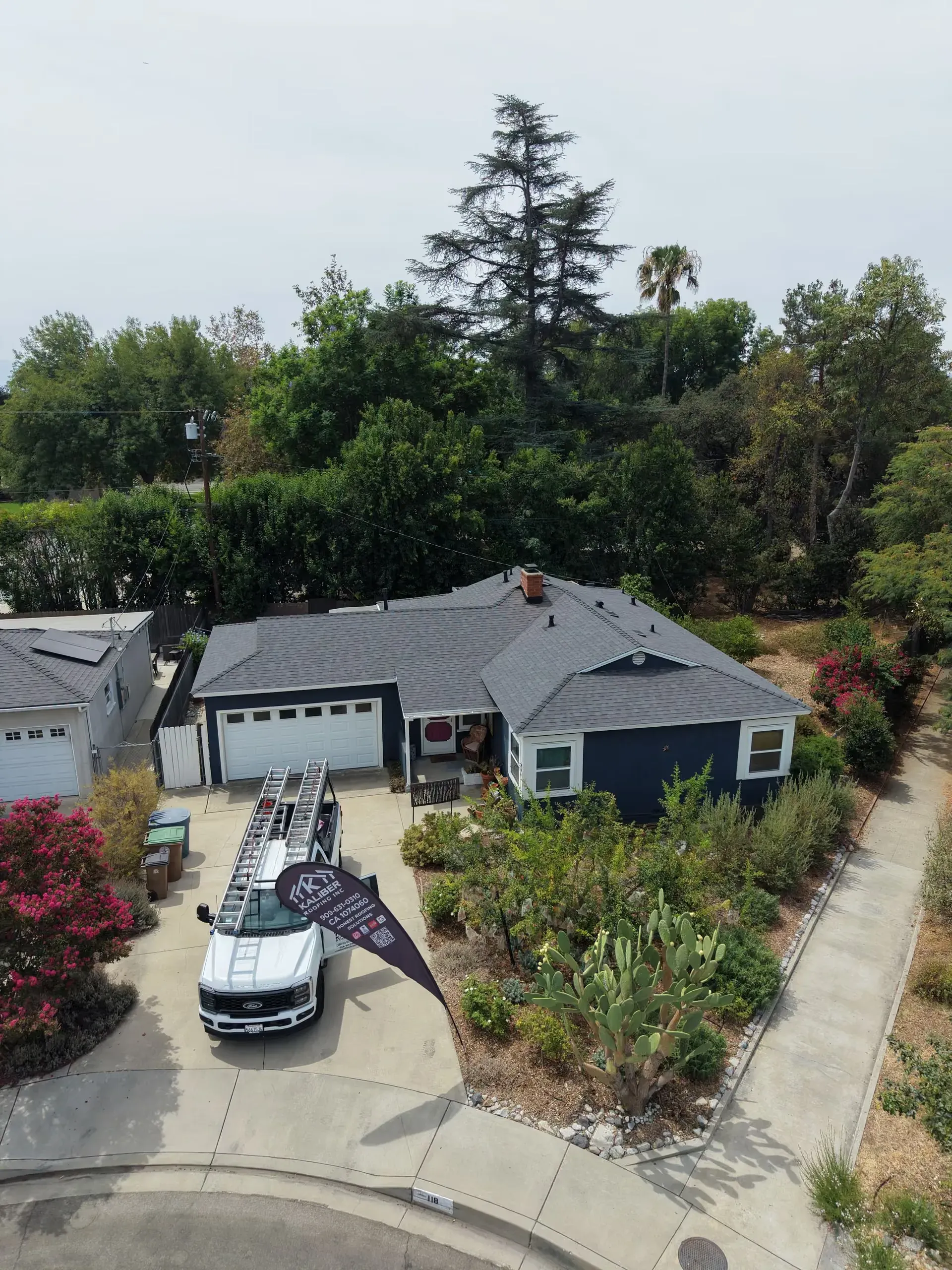 Aerial view of a gray house with a driveway, parked car, and landscaped yard in a suburban neighborhood