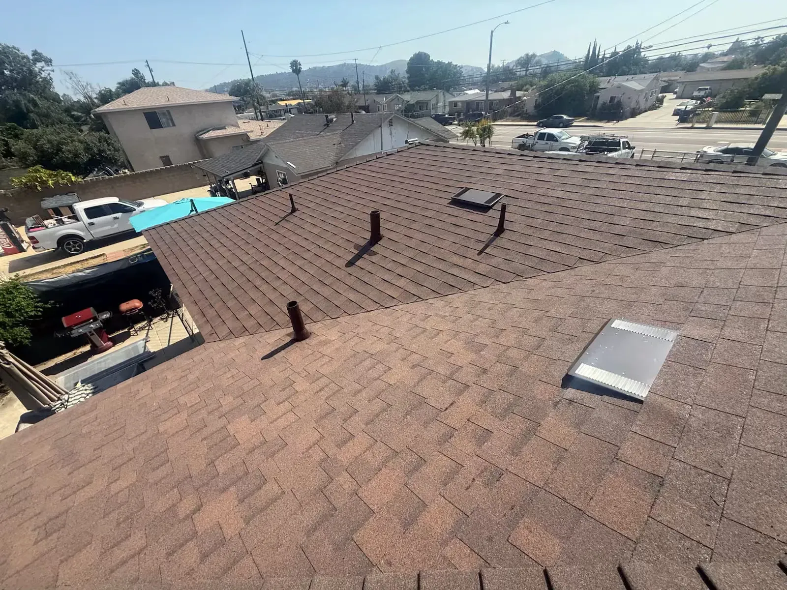Brown shingle roof with vents and a skylight, viewed from above in a suburban neighborhood