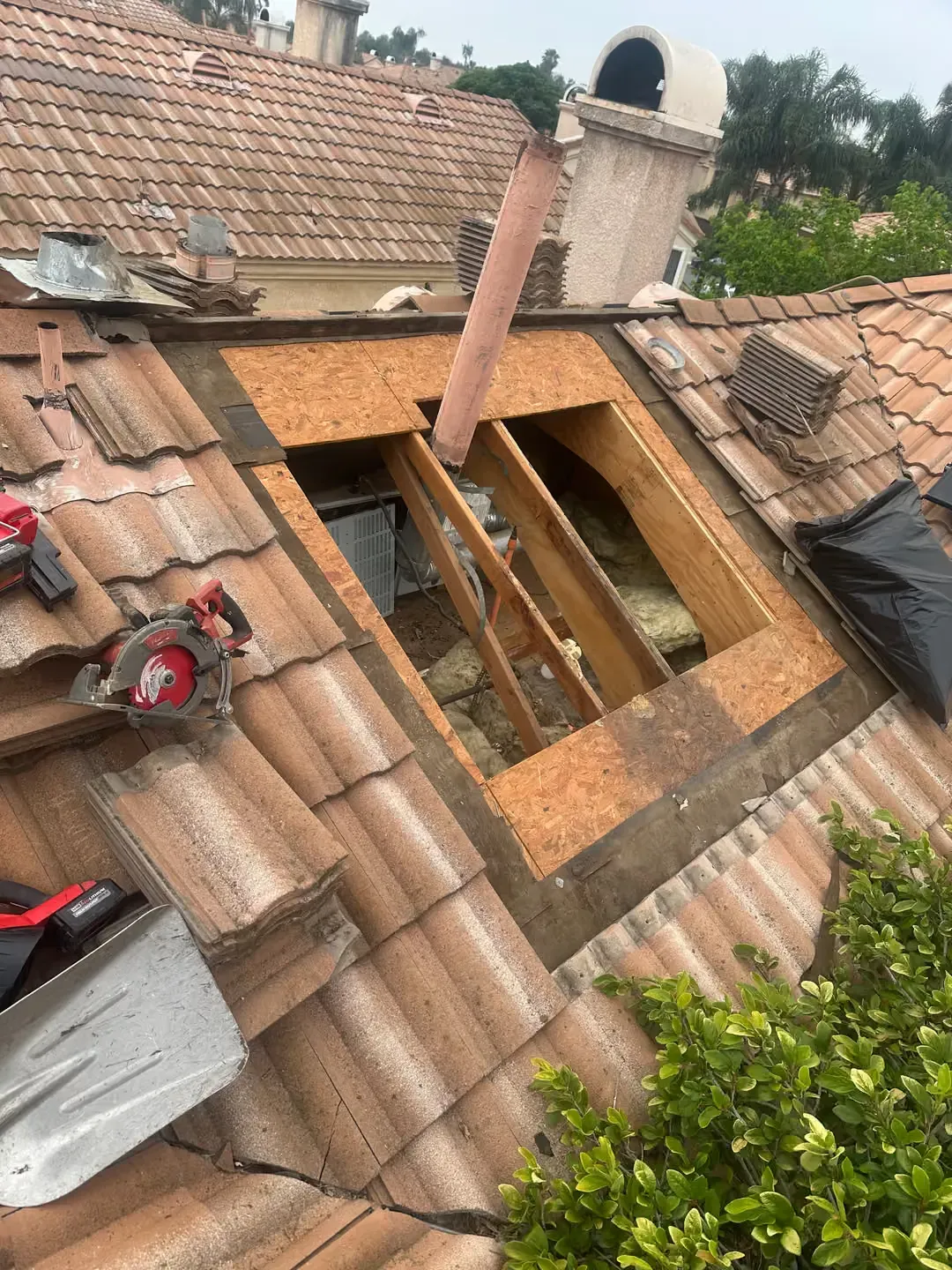 Damaged tiled roof with a large open hole exposing attic framing and a hanging pipe
