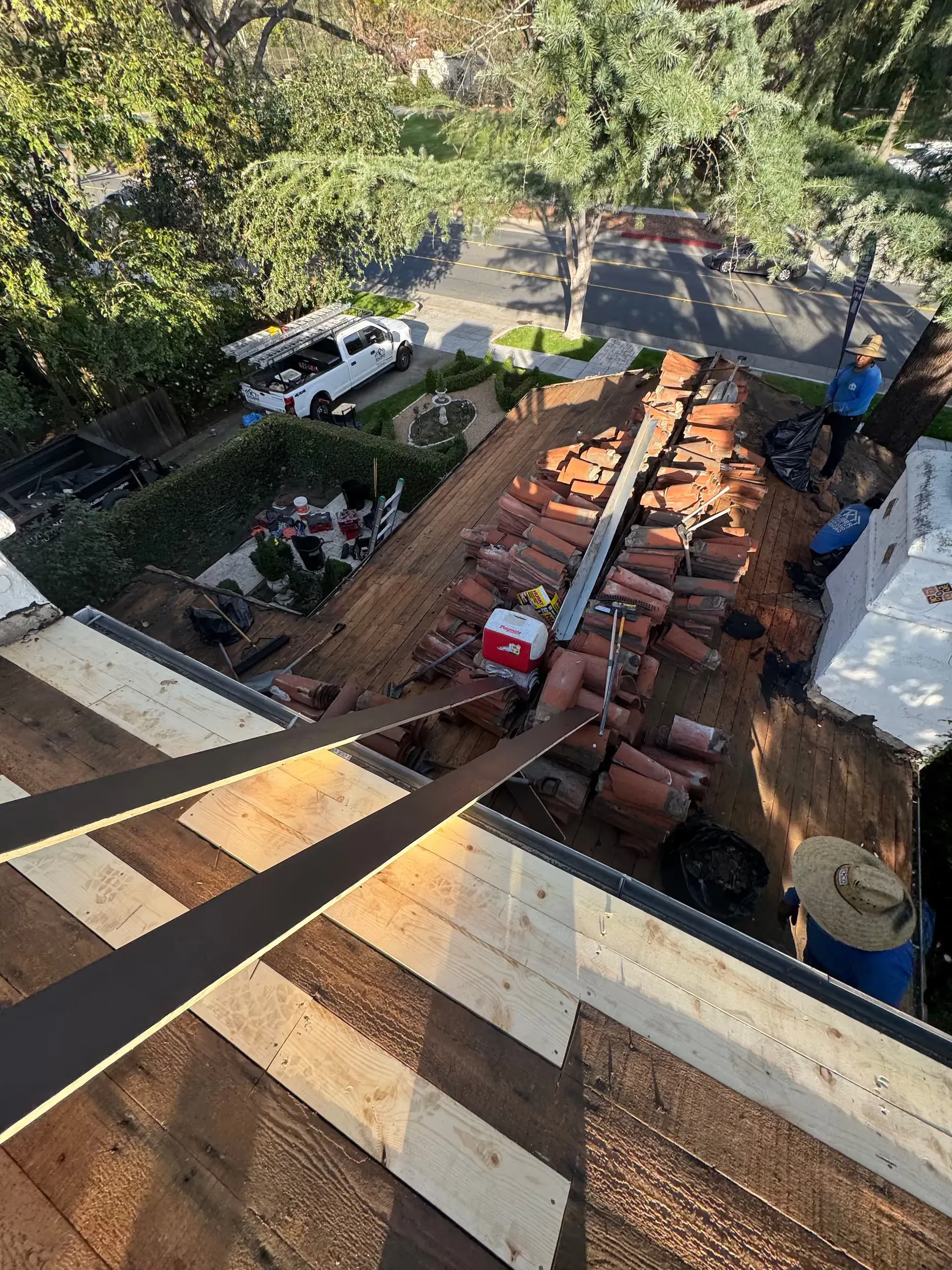 Rooftop construction site with stacked bricks, workers, and a white van below, seen from above.