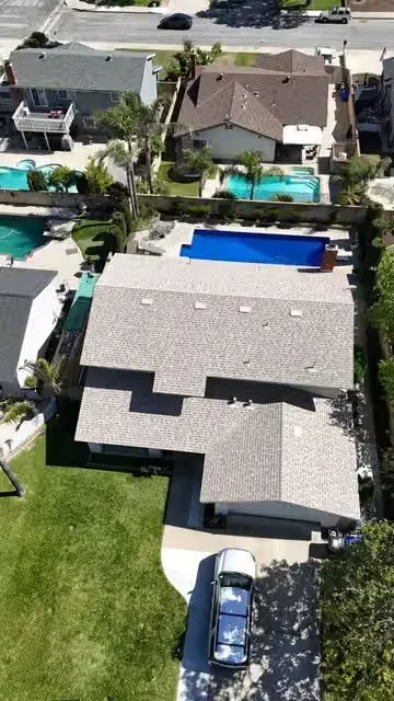 Aerial view of suburban houses with pools, lawns, and parked cars.