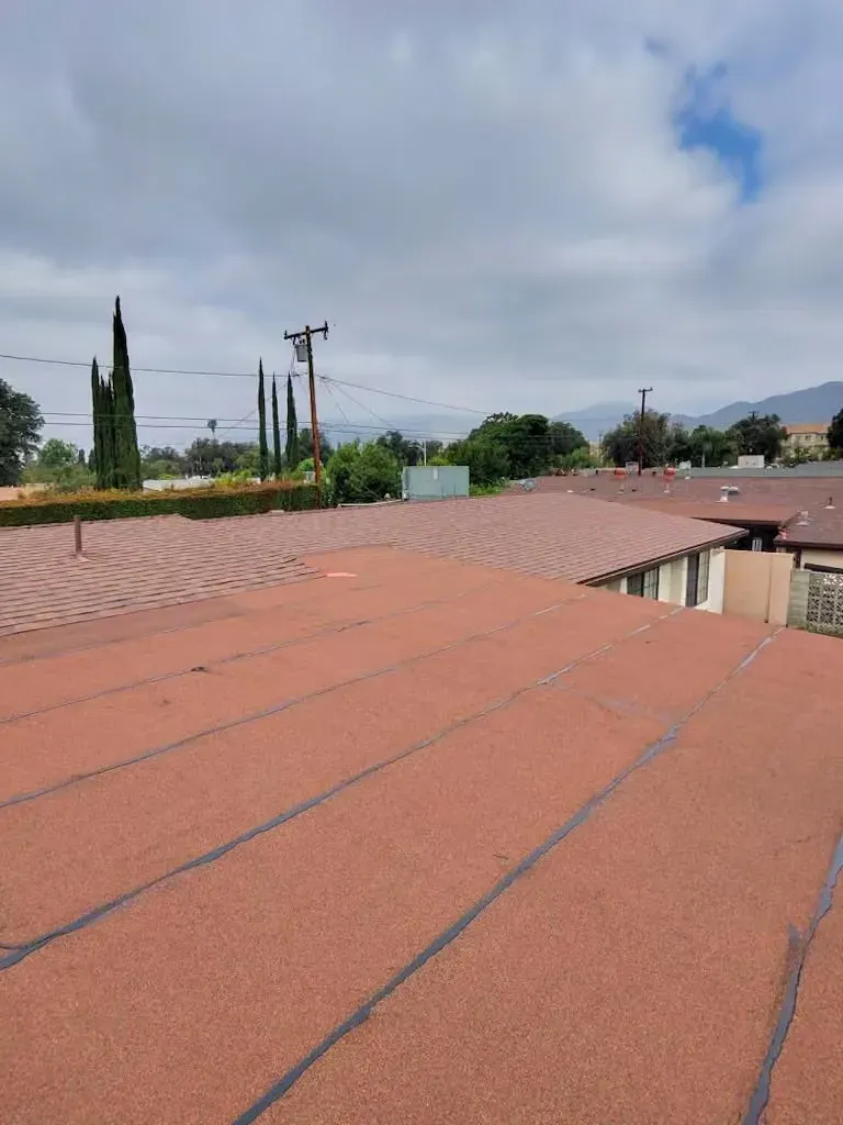 Rooftops with red tiles under a partly cloudy sky, with trees and utility poles in the distance