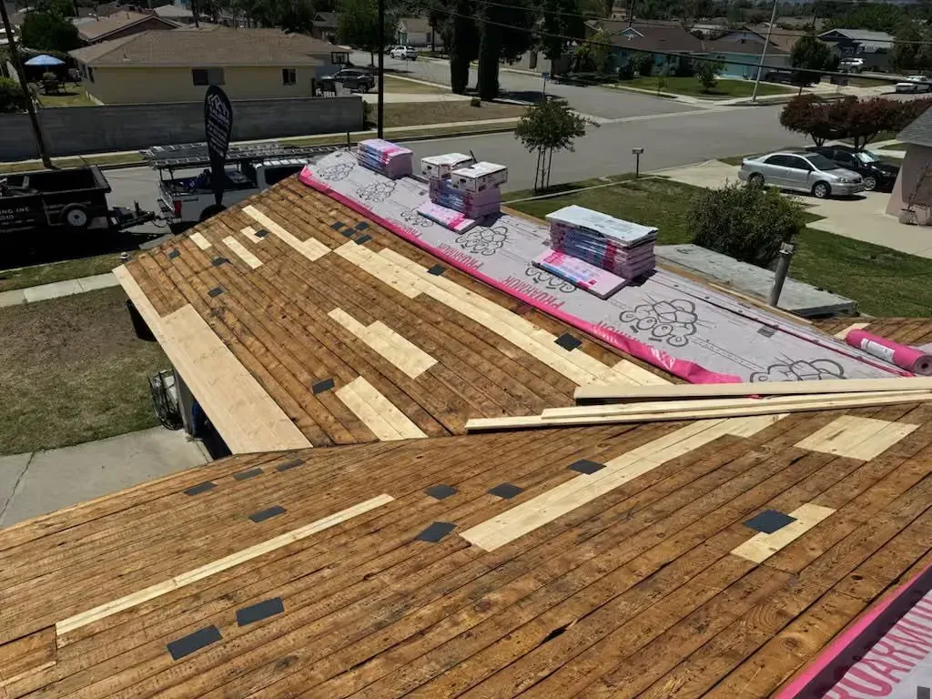 Roof under construction with plywood, pink underlayment, and workers on a residential house