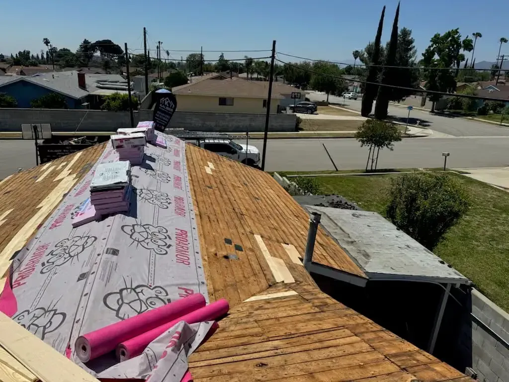 Roof under repair with pink foam boards and underlayment, overlooking a suburban street below