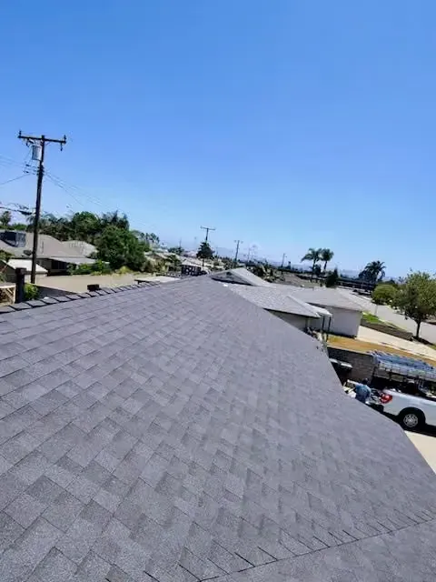 Rooftop shingles overlooking a sunny suburban street with houses, trees, and power lines