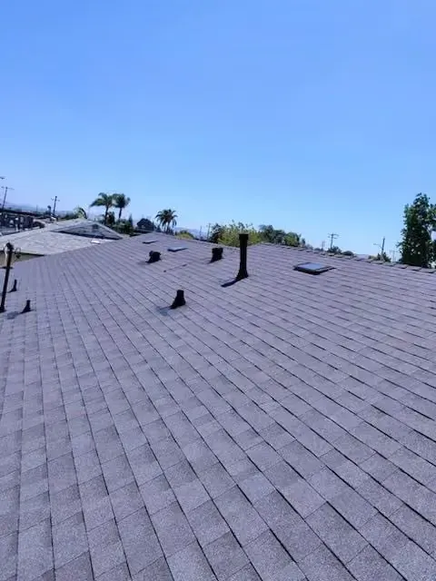Gray shingled roof with several black vents under a clear blue sky