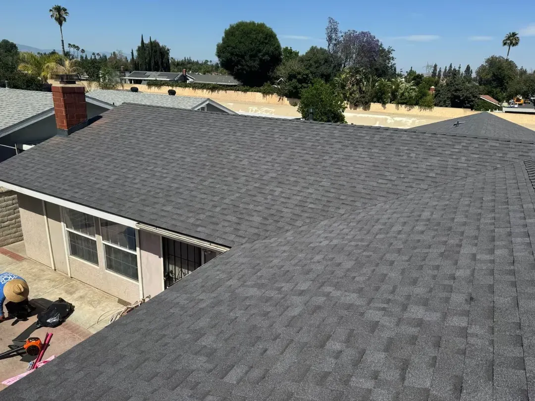 Gray shingled house roof with a worker visible at the lower left, viewed from above.