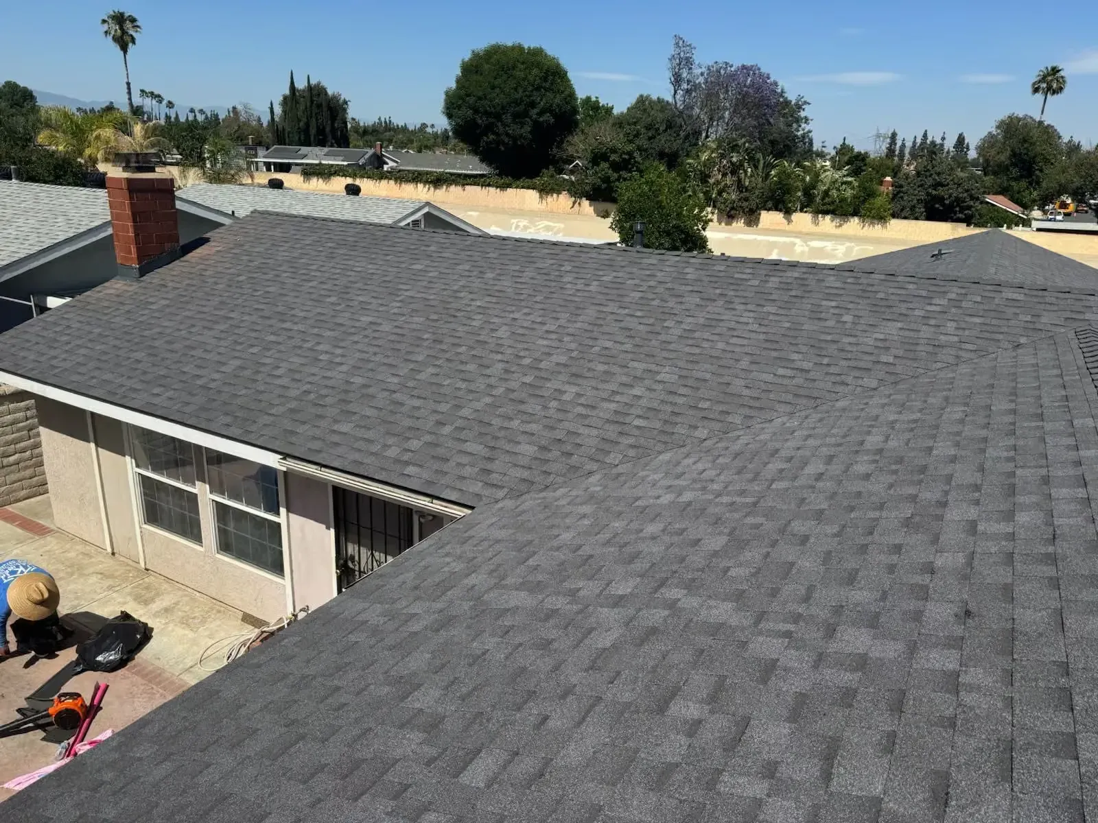 Gray shingled roof under construction with workers and tools on a sunny day
