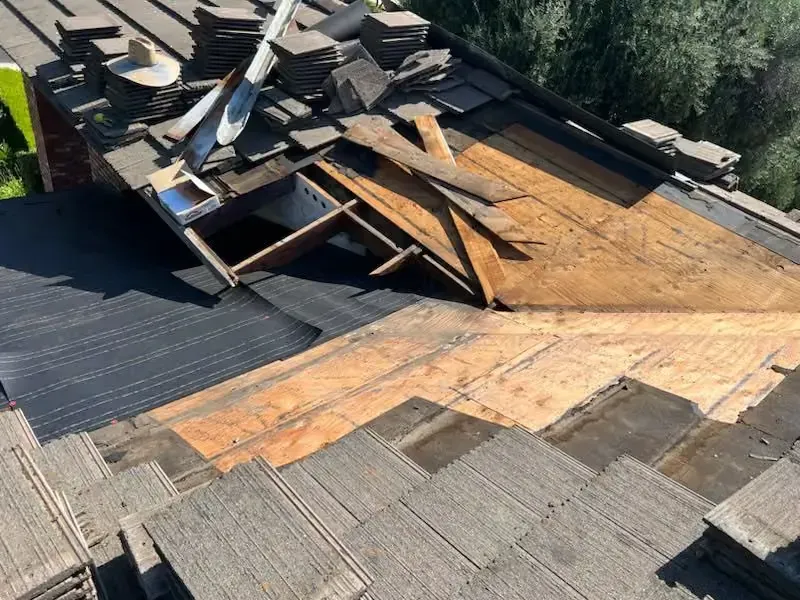 Damaged roof with missing shingles, exposed plywood, and scattered debris in a damaged section