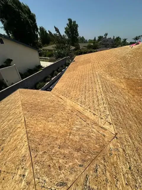 Roof deck under construction with OSB sheathing on a sloped rooftop in bright sunlight