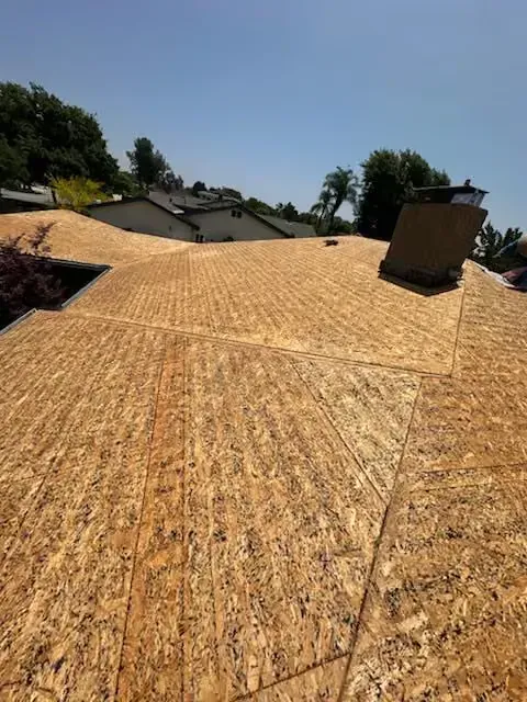 Rooftop under construction with plywood sheathing on a sunny day, viewed from above