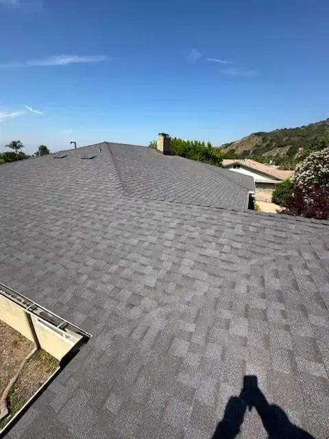 Gray shingled rooftop under a clear blue sky, with hills and nearby houses in the background