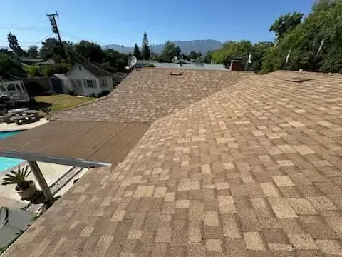 Wide tan shingle roof on a house, viewed from above with trees and neighboring homes in the background