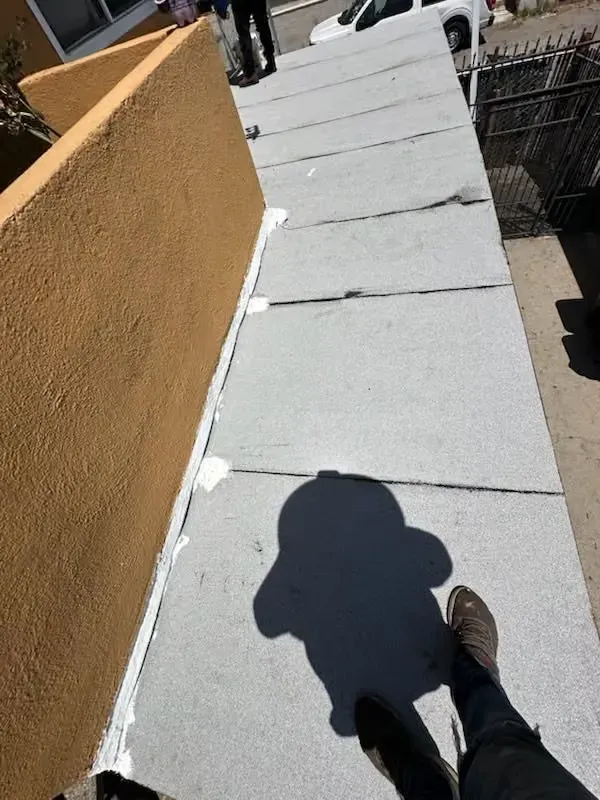 Walking along a narrow rooftop walkway with a tan wall and white floor panels in sunlight