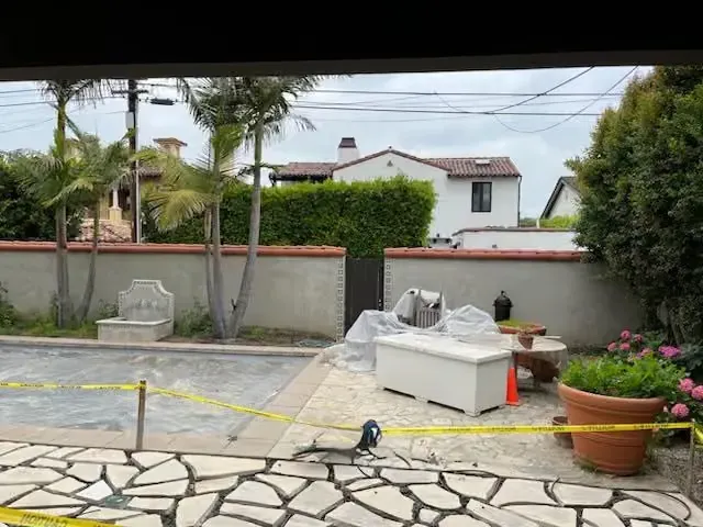 Patio with white bench, potted plants, and construction materials beside a wall and house.