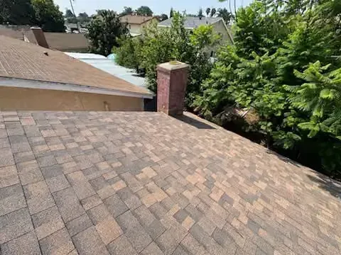 Rooftop with brown shingles, brick chimney, and green trees in the background
