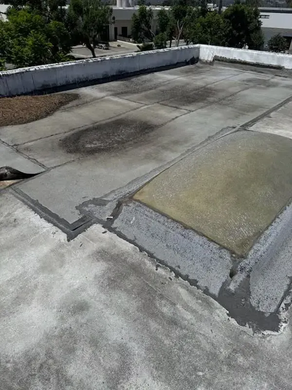 Damaged flat rooftop with patchwork repairs and cracked concrete near a low white parapet wall