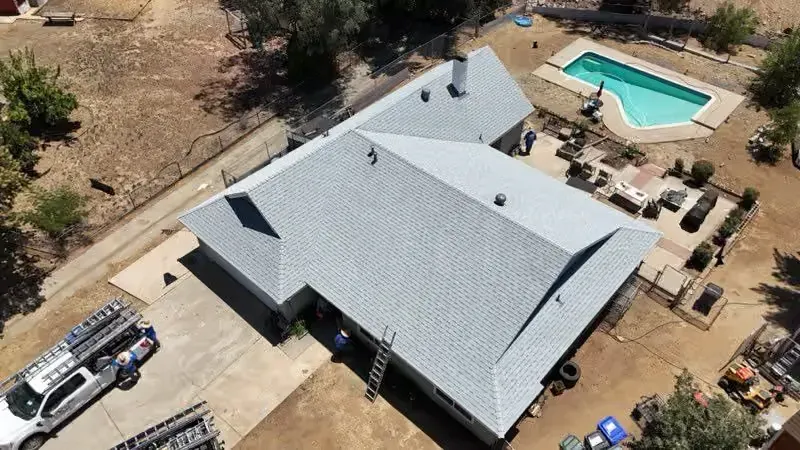 Aerial view of a gray-roofed house with a backyard pool, patio, and desert landscaping.
