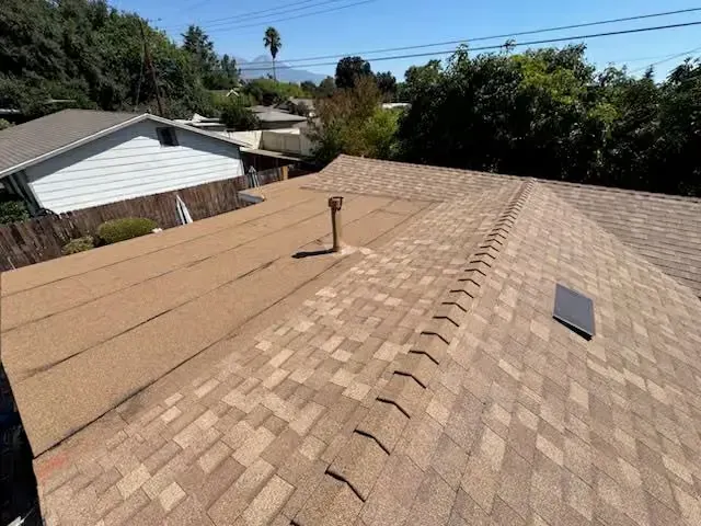 Residential shingle roof with vents under a clear blue sky, viewed from above