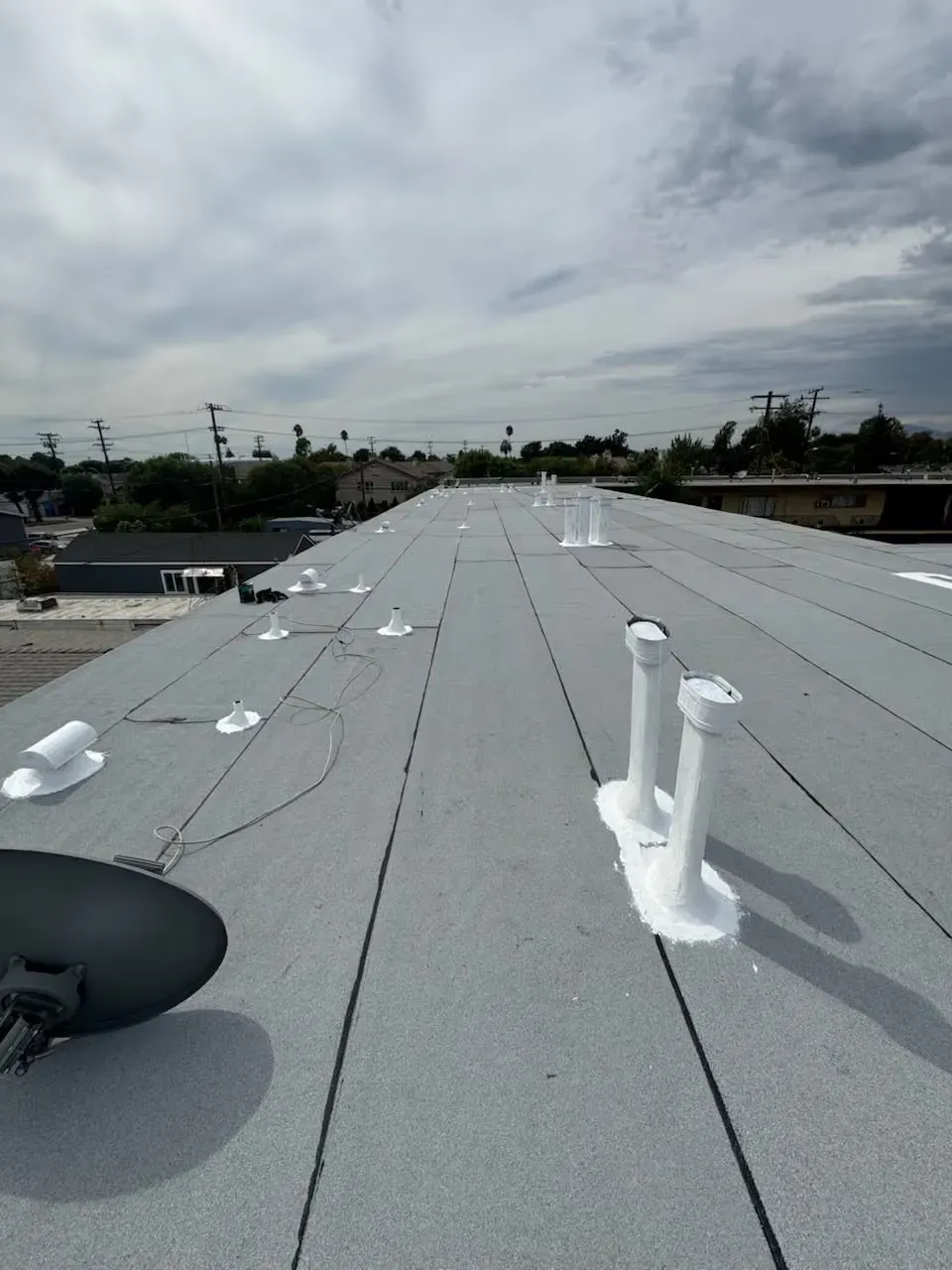 Rooftop with gray roofing, white vent pipes, and cloudy sky overhead