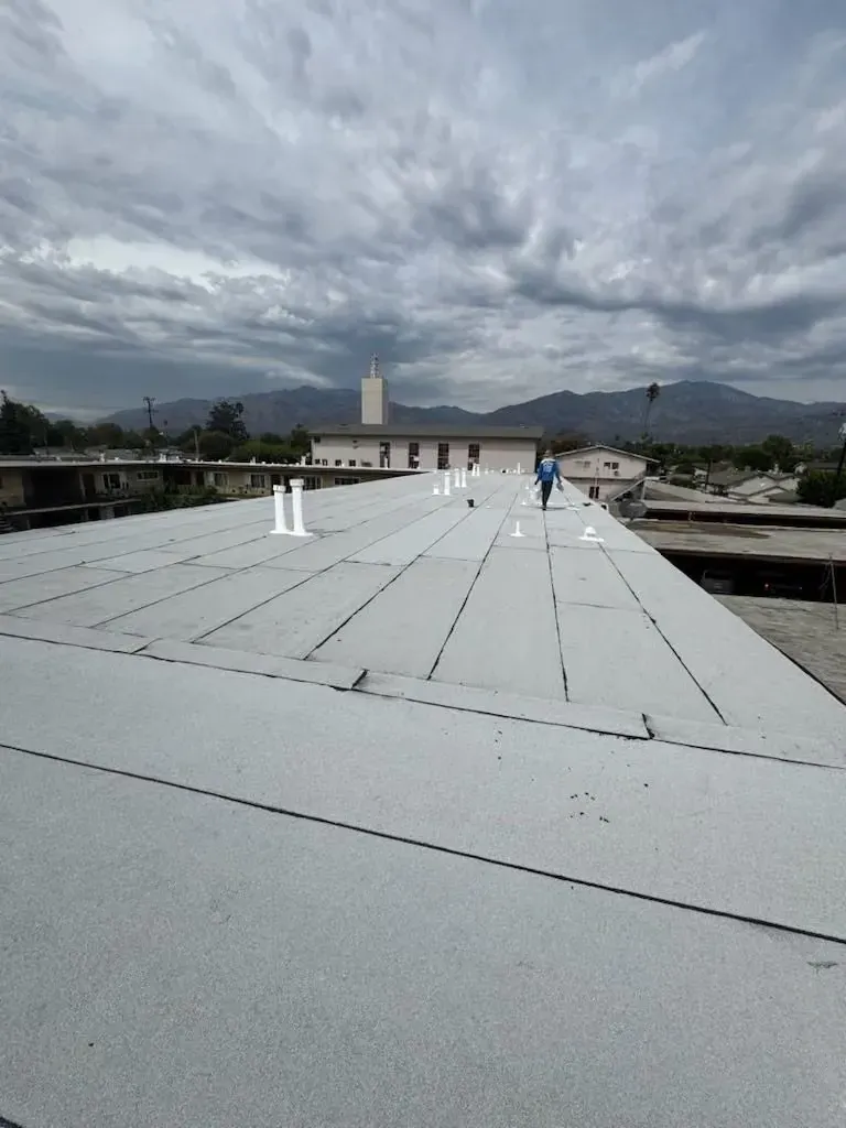 Rooftop with white membrane, workers in the distance, and cloudy mountains under an overcast sky