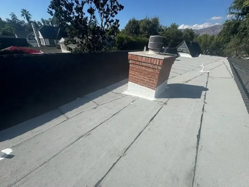 Flat rooftop with a brick chimney, vents, and a low black parapet under a clear sky.
