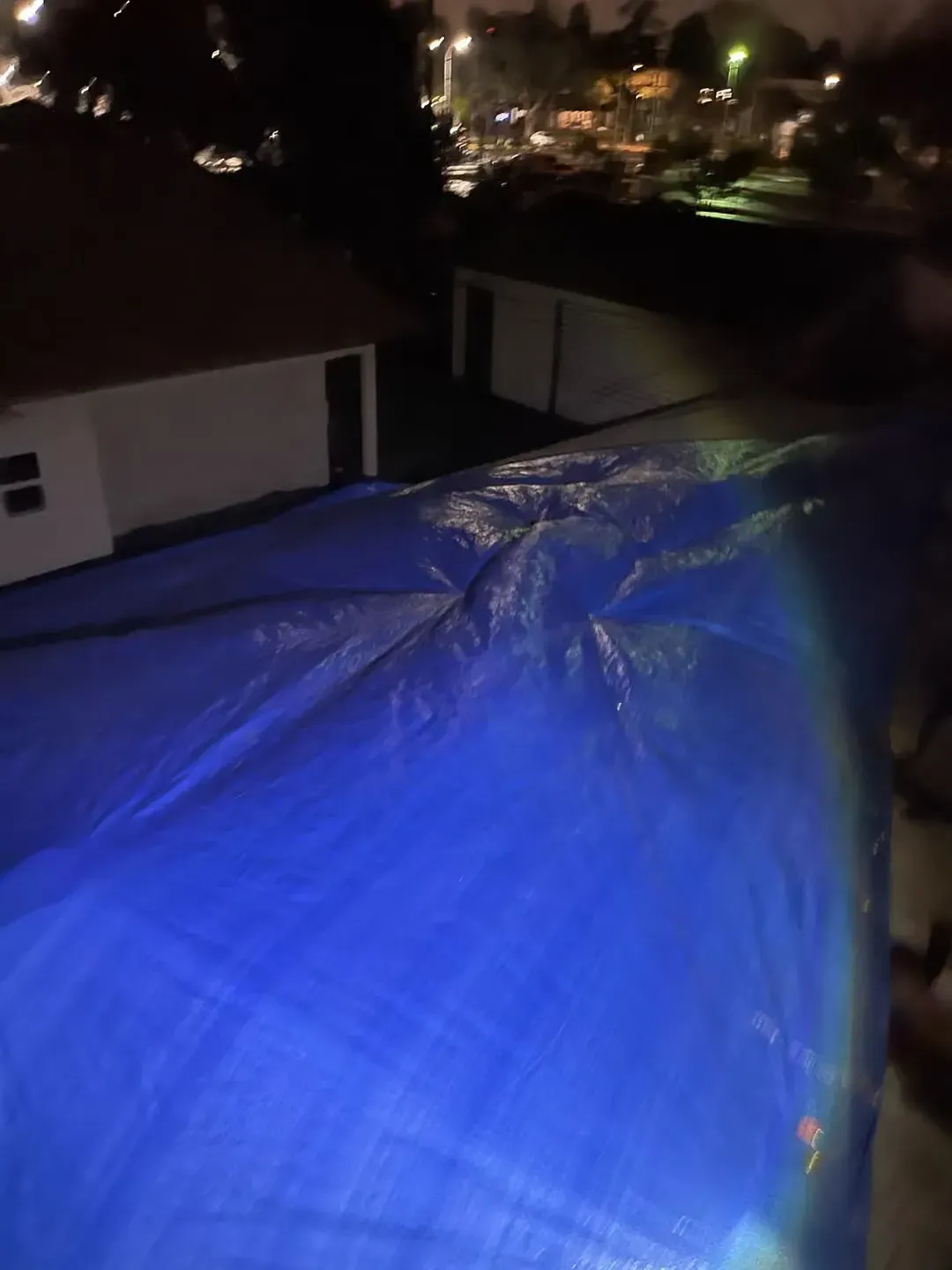 Blue tarp covering a rooftop at night, with buildings and lights in the background
