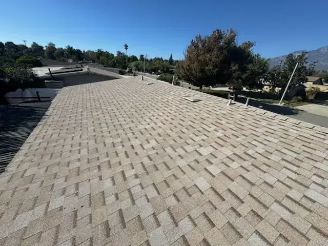 Wide beige rooftop with herringbone-patterned shingles under a clear blue sky.