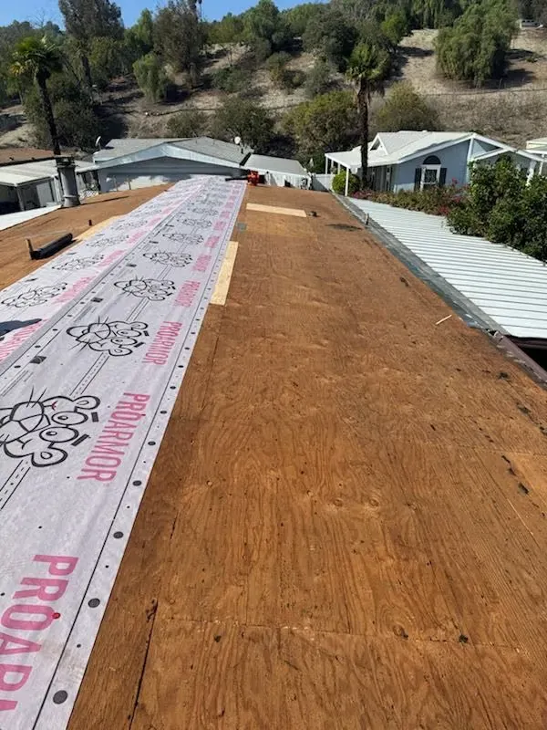 Roof under repair with pink underlayment running up the center, surrounded by brown plywood and hillside homes.